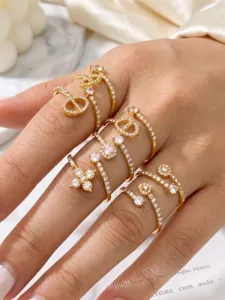 Close-up of stacked gold-tone rings with clear stones in geometric, floral and open designs
