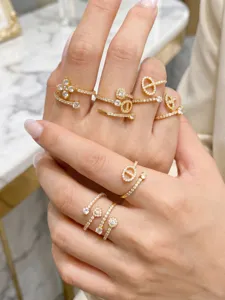 Close-up of hands wearing layered gold-tone rings with clear stones in floral and geometric designs