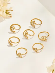 Overhead view of eight gold-tone rings with clear stones and varied openwork motifs