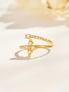 Gold open ring with clear stones and a flower-shaped cluster, photographed on a warm neutral surface