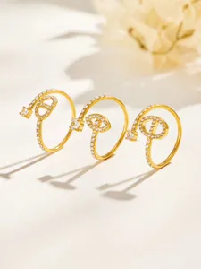 Three gold-tone rings with clear stones, displayed together against a softly lit cream background