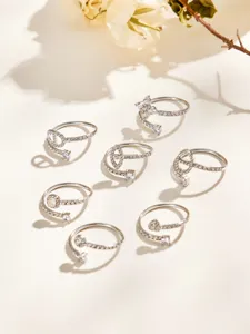 Silver-tone open rings with sparkling stones arranged on a warm cream surface beside dried flowers