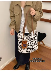 Person mit flauschiger weißer Tasche, schwarzen Flecken, braunen Henkeln und kleinem Bärenanhänger