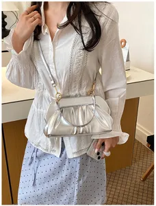La modella indossa una borsa argentata plissettata, con tracolla sottile e chiusura dorata