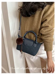 Dettaglio di una borsa a righe blu navy con patta in pelle, manico arcuato e pompon marrone