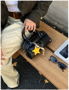 Borsa nera lucida con ciondolo a stella gialla sulla panchina di legno accanto agli occhiali da sole