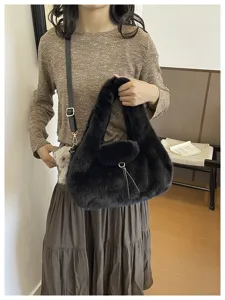 Black plush half-moon bag held by hand and worn crossbody, with a slim strap and metal clasp