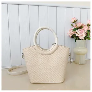 Sac crème à texture tressée, anse ronde et bandoulière réglable, présenté près de roses roses