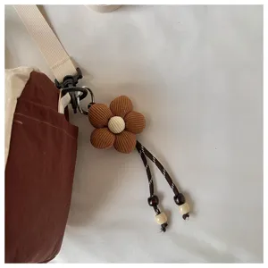 Ciondolo a fiore in tessuto marrone rigato, centro perlato color crema e cordoncini su una borsa