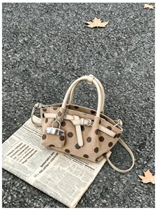 Borsa marrone a pois, manici color crema e ciondolo argentato appoggiata su un giornale