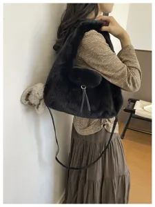 Side view of a model carrying a fluffy black shoulder bag with a long strap and tassel detail