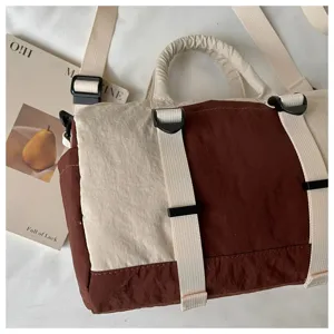 Dettaglio di una borsa in nylon bicolore con cinghie color crema, pannelli marroni e fibbie nere