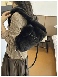 A woman wears a soft black faux-fur bag, showing its long strap and small gold-tone ring detail