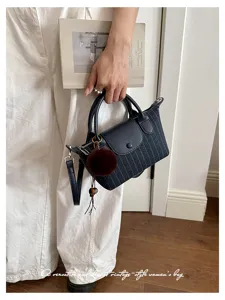Borsa a righe blu navy con manici in pelle, patta, pompon e tracolla, tenuta in mano da una persona