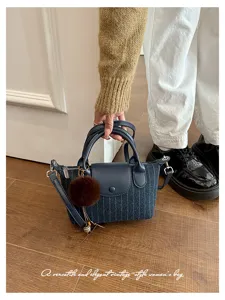 Borsa a righe blu tenuta in mano, con manici scuri e pompon marrone, sopra un pavimento in legno