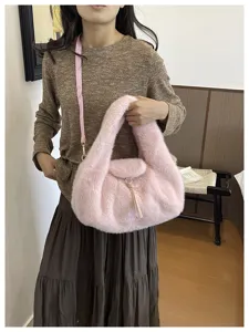 A model holds a soft pink crescent-shaped faux-fur bag with a slim strap and tassel charm