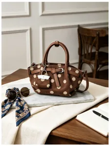Borsa marrone effetto camoscio a pois color crema, con manici in pelle e ciondolo metallico su un tavolo