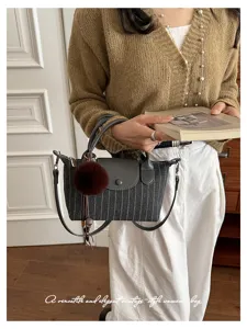 Donna con borsa grigio scuro a righe sottili, finiture in pelle e pompon marrone, in casa