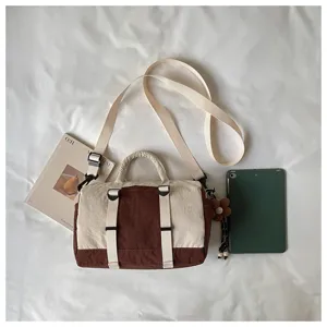 Vista dall'alto di una borsa beige e marrone con tracolla, ciondolo a fiore, libri e tablet