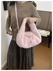 Soft pink plush half-moon bag shown on a model, with a long strap and gold-tone zipper detail