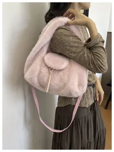 A model carries a soft pink faux-fur bag, showing its long shoulder strap and tassel detail