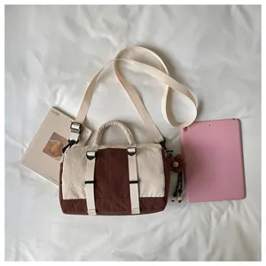 Borsa bicolore crema e bordeaux con tracolla e ciondolo, accanto a un libro e a un tablet rosa