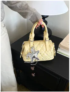 Dettaglio di borsa trapuntata giallo chiaro con strass e ciondolo a stella argentato, tenuta in mano