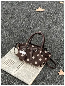 Dettaglio di borsa marrone effetto scamosciato a pois beige, con manici scuri e charm argentato