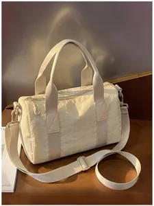Crèmekleurige nylon tas met dubbele handgrepen, afneembare schouderband en rits, op een tafel