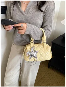 Dettaglio di borsa giallo chiaro trapuntata, con strass e ciondolo a stella argentato, portata a mano
