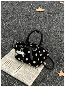 Borsa nera a pois beige, manici in pelle e ciondolo a lucchetto argentato su asfalto