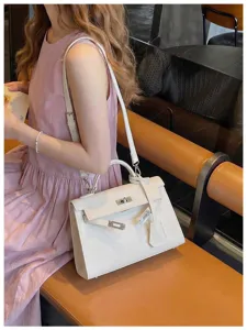 Borsa bianca strutturata su una seduta di un caffè, con chiusura argentata, tracolla e ciondolo