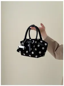 Dettaglio di una borsa nera a pois bianchi tenuta in mano, con manici in pelle e dettagli argentati