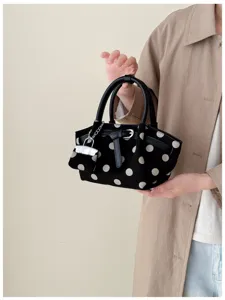 Una persona tiene una borsa nera a pois bianchi, con manici in pelle e un ciondolo argentato