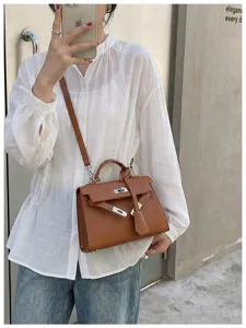 Borsa marrone goffrata, chiusura argentata e tracolla rimovibile, portata su camicia bianca