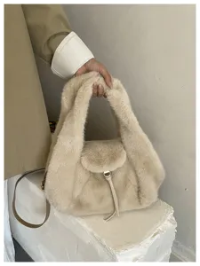 Close-up of a hand holding a soft ivory faux-fur bag with a flap, metal clasp and slim strap