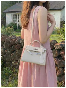 Borsa avorio con superficie goffrata e dettagli argentati, indossata con un abito rosa in giardino
