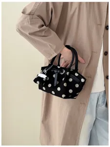 Borsa in tessuto nero a pois bianchi portata da una modella, con manici in pelle e piccolo ciondolo