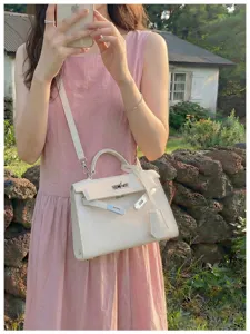 Borsa color crema in pelle goffrata con dettagli argentati, portata a tracolla davanti a un giardino