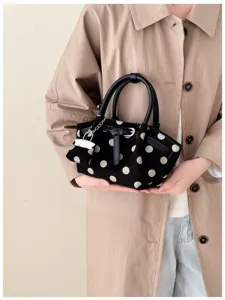 Borsa nera a pois avorio tenuta da una modella, con doppi manici e ciondolo a catena argentato