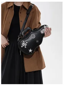 Détail d’un sac noir en forme de guitare, avec motifs brodés et bandoulière porté par un modèle