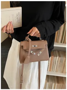 Borsa marrone in similpelle martellata, con chiusura metallica e tracolla regolabile accanto ai libri