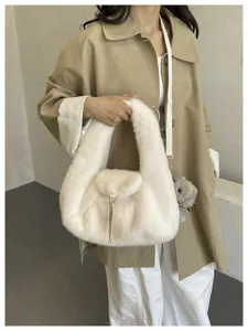 Model carrying a plush ivory bag, showing its rounded shape, flap clasp, tassel charm and strap