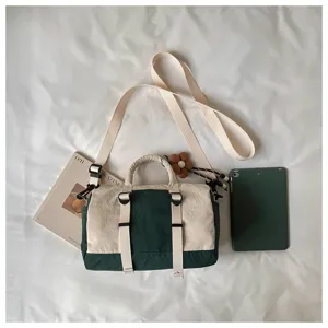 Vista dall’alto di una borsa avorio e verde scuro, con tracolla larga in tessuto e fibbie metalliche