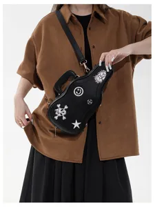 Una persona indossa una borsa nera a forma di chitarra, con toppe ricamate e tracolla regolabile.