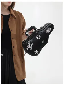 Borsa nera a forma di chitarra tenuta da una modella, con toppe ricamate, zip e catena metallica