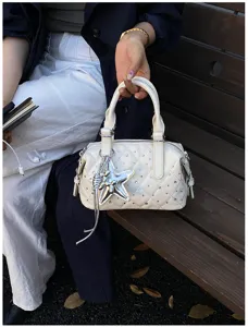 Dettaglio di una borsa avorio trapuntata, con strass, ciondolo a stella argentato e catena pendente