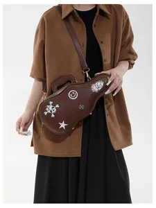 Sac brun en forme de guitare, brodé de crâne et d’étoiles, porté avec une bandoulière réglable.