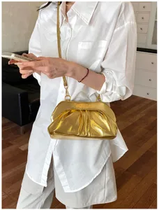 Borsa dorata lucida e arricciata, con tracolla sottile, indossata sopra un look bianco