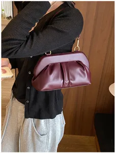Borsa bordeaux arricciata con chiusura dorata, indossata sopra un maglione nero a coste
